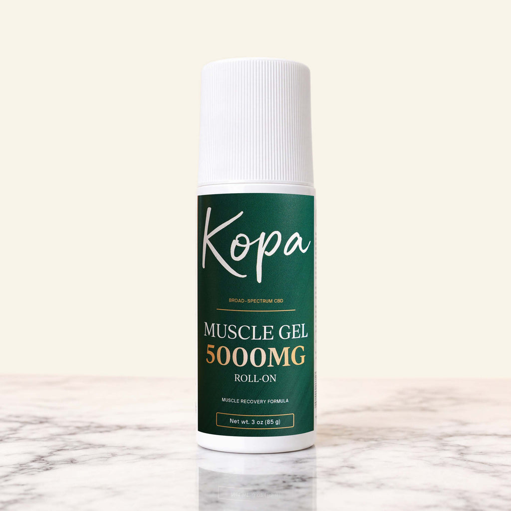 Kopa Muscle Gel Roll-On 5000mg CBD in a white bottle with a dark green label, cap on, standing on marble
